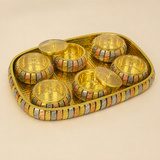 A gold-toned decorative tray holding six small round gold vessels with lids, photographed on a plain warm beige background.