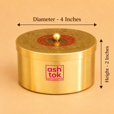 Product dimension diagram showing the cylindrical Ashtok brass box. Measurement arrows indicate a diameter of 4 inches across the top lid and a height of 2 inches along the side. The brass container has a brushed metallic body with the Ashtok brand logo on the front and an intricately engraved gold and red patterned lid topped with a spherical gold knob.