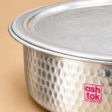 Close-up product photograph of an Aluminium Biryani Handi with Lid highlighting the detailed hammered exterior surface, smooth circular lid, broad rolled rim and reflective silver aluminium finish. The enlarged view reveals the closely arranged circular hammered impressions across the cooking vessel body, along with the fine texture of the matching metal lid and neatly finished rim. Warm beige studio lighting enhances the silver metallic surface while maintaining natural reflections and visible product.