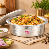 raditional Aluminium Biryani Handi filled with freshly prepared Hyderabadi chicken biryani featuring aromatic long-grain basmati rice, golden saffron-coloured rice, seasoned chicken pieces, fried onions and fresh green coriander garnish. The matching aluminium lid is positioned behind the cooking vessel, revealing the delicious biryani inside. The handi features a hammered silver metallic.