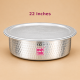 22 inch Aluminium Biryani Handi with Lid displayed from a front three-quarter perspective against a clean beige studio background. The handi has a wide circular opening, matching flat aluminium lid, hammered silver exterior and smoothly curved lower body. Its traditional rounded construction and textured metallic surface give it the classic appearance of an Indian cooking vessel used for biryani preparation. Suitable for preparing Hyderabadi dum biryani, aromatic rice dishes, pulao and food for family.