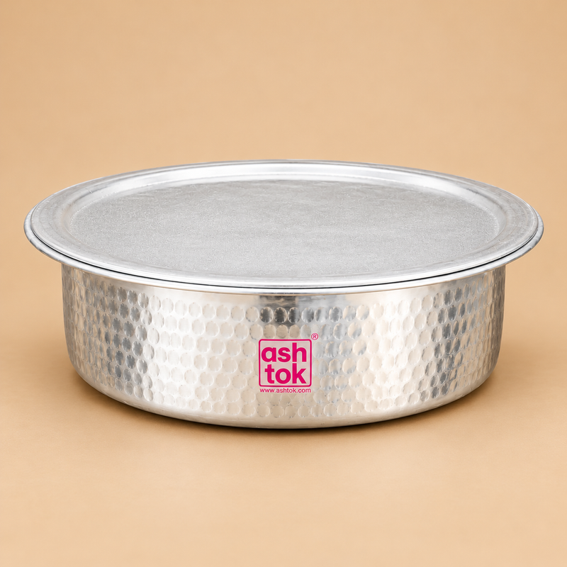 Traditional Aluminium Biryani Handi with Lid featuring a wide circular cooking vessel, distinctive hand-hammered silver aluminium exterior, smooth rounded base and matching flat circular metal lid. The handi has a broad rolled rim and evenly distributed circular hammered patterns across its outer body, giving it a classic Indian cookware appearance. Photographed from a front three-quarter angle against a warm beige studio background with soft lighting and natural shadows