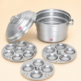 Ashtok aluminium idli steamer pot set with a lifted lid and three interchangeable idli plates containing 7, 5, and 4 cavities arranged in front.