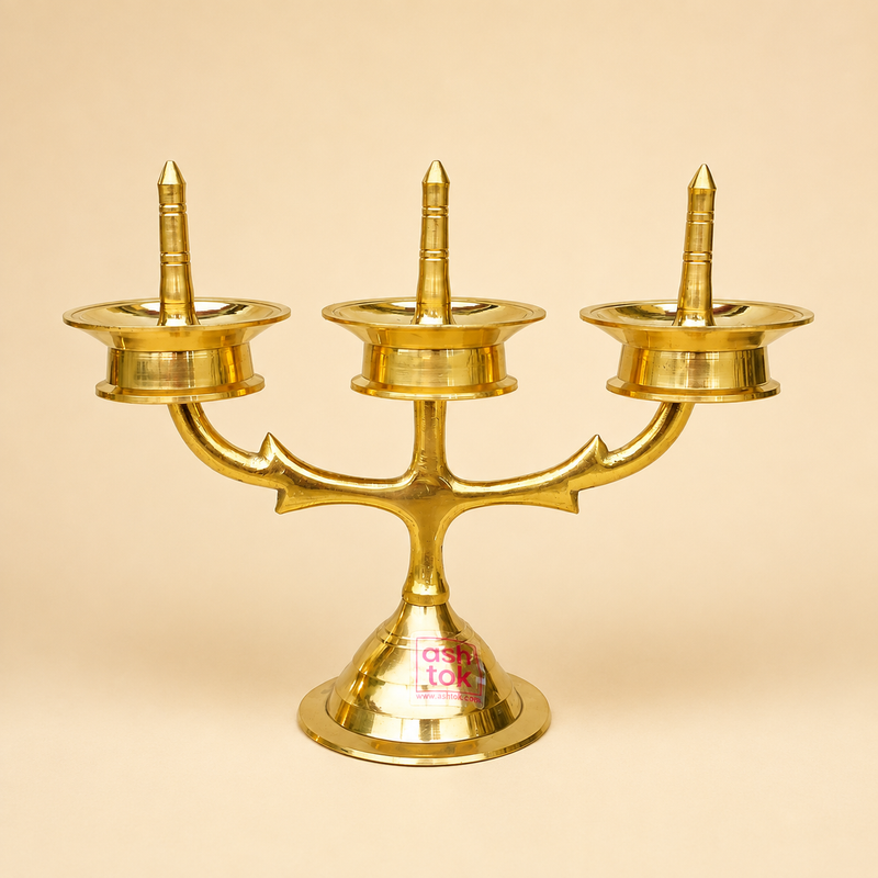 Ashtok traditional 3-face brass diya stand or Kuthu Vilakku with three oil cups and central wick spikes on a polished pedestal base.