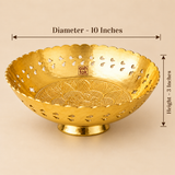 Dimension diagram for the Ashtok brass decorative bowl against a warm studio background. Measurement arrows indicate a top diameter of 10 inches across the scalloped rim and a height of 3 inches from the pedestal base to the top rim. The bowl features pierced side cutouts and an embossed floral medallion base with the Ashtok brand label inside.