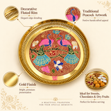 An informative marketing graphic highlighting key features of the Ashtok brass decorative tray. Four visual callouts emphasize the "Decorative Fluted Rim" with elegant edge detailing, "Traditional Peacock Artwork" featuring festive handcrafted enamel appeal, a bright "Gold Finish", and an inset photo showing the tray filled with sweets, chocolates, and dry fruits titled "Ideal for Sweets, Chocolates & Dry Fruits".