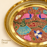 Close-up detail photograph highlighting the intricate craftsmanship of the Ashtok brass tray. The image focuses on the raised fluted brass border and the detailed enamel inlay work showing a peacock's detailed blue and teal feathers, floral motifs, and fine textured red pattern background, with "Premium Detail" printed in the bottom left corner.