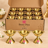 Ashtok brass diya 12 pcs box pack image showing twelve polished brass diyas arranged inside a partitioned box with three brass diyas displayed in front on a warm beige background.