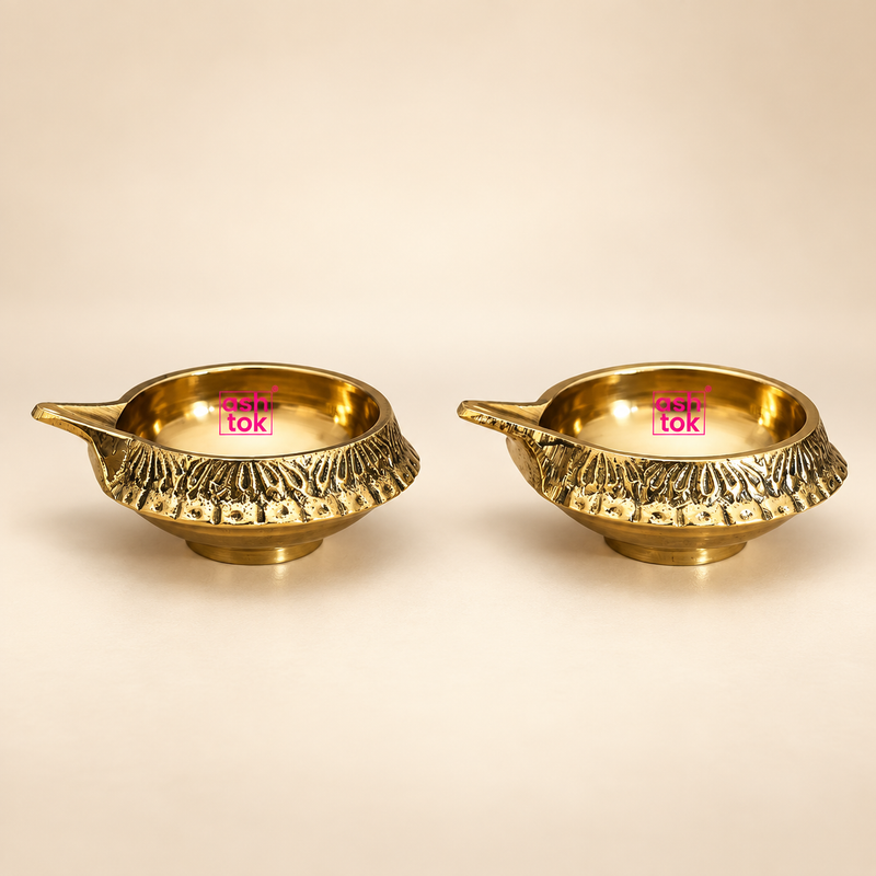 ASHTOK brass diya pack of 2 with decorative textured outer design and polished brass finish, displayed on a clean beige background for pooja, gifting and festive decor use.