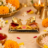 Lifestyle image of Ashtok brass double duck sindoor box used in a festive pooja setting, with one side filled with red kumkum and the other with rice grains, surrounded by flowers, brass pooja decor, and a warm devotional background.