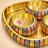 Close-up detail of ASHTOK brass gift tray and bowls showing the polished golden hammered surface, decorative gold copper and silver-toned embossed pattern, matching lidded bowls, detailed knobs and pink ASHTOK branding on the lid.