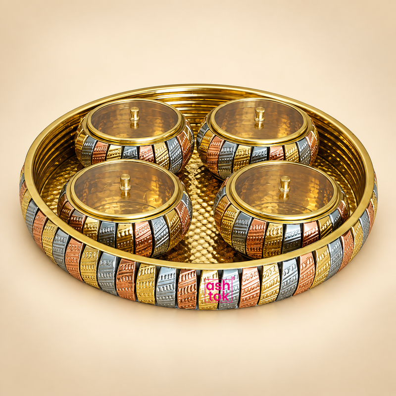ASHTOK brass gift tray set with 4 matching lidded bowls featuring a decorative multi-tone gold, copper and silver finish, hammered brass-style tray surface and pink ASHTOK logo, displayed on a clean warm beige background for gifting and serving use.
