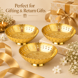 Promotional gift setting image featuring three Ashtok brass decorative bowls arranged on a warm beige surface with white jasmine flowers, a golden ribbon, and a wrapped gift box with a satin bow. A lit brass diya glows in the soft-focus background. Headline text reads "Perfect for Gifting & Return Gifts".