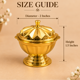 Size guide infographic for the Ashtok brass kumkum box, featuring a closed gold-tone brass container with a carved fluted lid on a pedestal base. Overlay lines with measurement arrows indicate a top diameter of 2 inches and a total height of 1.5 inches.