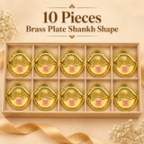 Ten piece gift pack image of the Ashtok brass plate shankh shape displayed inside a long premium beige presentation box with individual compartments. Each of the ten brass plates has the same polished golden brass finish, scalloped rim, embossed traditional detailing and shankh-inspired shape, with the pink Ashtok branding visible on every piece. The layout presents the products in an organized and elegant format, making the image suitable for customers looking for bulk gifting, wedding return gifts, festiv