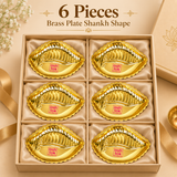 Six piece gift set image of the Ashtok brass plate shankh shape arranged neatly inside a premium beige box with cushioned compartments. Each plate is identical in size and shape, featuring a polished golden brass finish, traditional shankh design, scalloped border, embossed inner detailing and the original pink Ashtok logo at the center. The six plates are placed carefully inside a presentation box, making this pack ideal for return gifts, wedding favors, festive hampers, traditional gifting, pooja gifting,