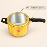 High-angle product shot of an open Ashtok brass pressure cooker pot against a light beige background. The exterior of the pot is polished yellow brass stamped with a red "ashtok" brand logo on the lower front body. The interior is coated with a shiny silver-toned finish, pointed out by a curved black callout line pointing to a label in the top right that reads "Tin Lined (Kalai) Coating". The body is fitted with a short black side grip handle on the left and a long black ergonomic main handle on the right w