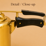 Detailed close-up of the black heat-resistant Bakelite handle, locking mechanism, and brass body bracket on an Ashtok pressure cooker.