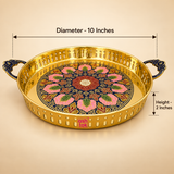 ASHTOK brass round serving tray size guide showing 10 inch diameter and 2 inch height, featuring a polished golden brass finish, decorative multicolor floral center design, perforated side rim and ornate blue dual handles for serving and gifting.