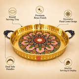 ASHTOK premium brass round serving tray with decorative floral center artwork, polished golden brass finish, perforated side border and ornate dual blue handles, designed for serving snacks, sweets, beverages, festive refreshments and decorative table display.