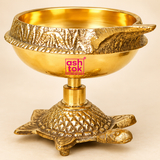 Close-up image of a brass diya with a textured turtle-shaped base, highlighting the polished golden finish, bowl shape, craftsmanship, and intricate detailing on a beige background.