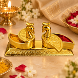 Traditional lifestyle image of the brass twin peacock haldi kumkum box styled in a festive and devotional setting on a warm beige surface. The product is presented as a decorative pooja accessory suitable for storing haldi and kumkum during rituals, religious functions, festive celebrations, wedding ceremonies and housewarming events. The twin peacock form, golden polished brass surface and elegant carved detailing make it a visually rich decorative piece that blends well with traditional Indian styling. Th