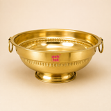 Ashtok traditional brass urli bowl featuring a raised pedestal base, side ring handles, and decorative ribbed detailing.