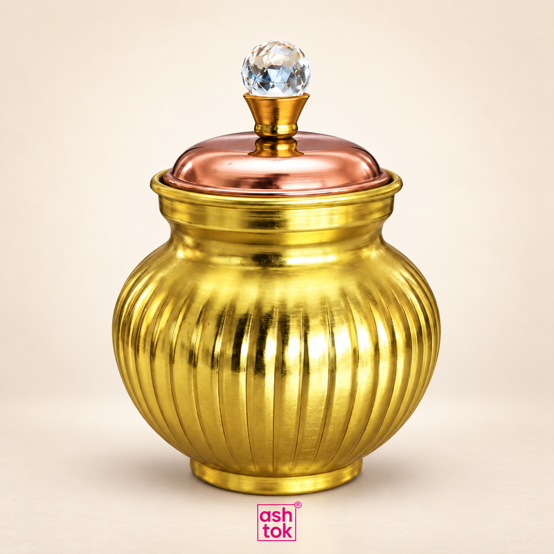 Ashtok chocolate box surai gift item in a clean beige studio setting, featuring a decorative round brass-finish storage jar with vertical ribbed detailing, a warm copper-toned lid, and a faceted crystal-style knob on top. The product is shown as a standalone hero image with soft lighting and a neat shadow, clearly highlighting the elegant shape, polished metallic finish, rounded body, and premium handcrafted appearance. This decorative gift box style surai is ideal for festive gifting, storing chocolates or