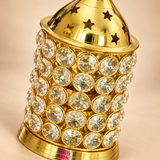 Close-up detail image of the ASHTOK Crystal Diya Brass focusing on the upper and middle sections of the product. The photograph clearly shows the polished brass dome with star-shaped cutouts, the fine reflective metal finish, and the crystal-studded cylindrical body made of round clear stones set in a metal frame. This detailed close-up highlights the craftsmanship, premium materials and decorative appeal of the diya, making the sparkle, texture and finishing clearly visible.