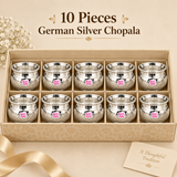 Pack of 10 Ashtok German Silver Chopala Haldi Kumkum Boxes displayed in an elegant beige compartmentalized presentation box with ten identical polished silver-finish bowls arranged neatly in two rows. Each German silver chopala has a wide flared rim, rounded decorative body, intricate embossed floral design, smooth reflective finish and original pink Ashtok branding. This 10 piece set is suitable for wedding return gifts, haldi kumkum ceremonies, festive giveaways, religious functions, traditional family ev