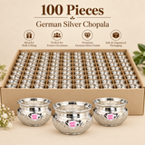 Bulk pack presentation of 100 Ashtok German Silver Chopala Haldi Kumkum Boxes arranged in a large organized compartmentalized carton for wholesale, event and large-scale gifting requirements. The image shows numerous identical polished German silver chopalas securely packed in individual sections, along with larger close-up bowls displayed in the foreground to clearly show the wide flared rim, rounded body, intricate embossed floral detailing, reflective silver finish and original pink Ashtok logo. This 100