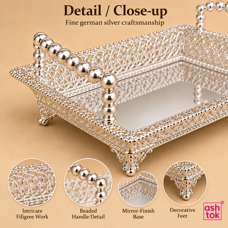 Close-up detail image of the Ashtok German silver fancy tray highlighting the delicate filigree craftsmanship, polished silver finish, textured ornamental edgework, bead-style side handle detailing, small raised decorative legs, and reflective tray base, giving a clear view of the fine handcrafted look and premium finishing that make this tray suitable for elegant serving and gifting.