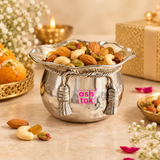 ASHTOK German Silver handi and sweet bowl styled in an elegant festive serving setup and filled with assorted dry fruits including almonds, cashews, pistachios and raisins. The polished silver bowl with hammered body, scalloped rim, decorative rope band and tassel ornaments is presented with warm festive décor, flowers and gifting elements, demonstrating its use for sweets, dry fruits, festive serving, celebrations and premium gifting.