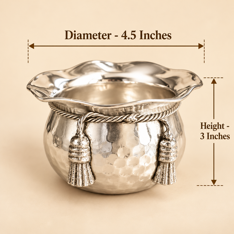 ASHTOK German Silver handi and size guide diameter 4.5 inches height 3 icnhes sweet bowl styled in an elegant festive serving setup and filled with assorted dry fruits including almonds, cashews, pistachios and raisins. The polished silver bowl with hammered body, scalloped rim, decorative rope band and tassel ornaments is presented with warm festive décor, flowers and gifting elements, demonstrating its use for sweets, dry fruits, festive serving, celebrations and premium gifting.