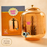 Ashtok 16-litre hammered copper water matka dispenser with brass knob lid and chrome tap, displayed alongside its branded orange packaging box.