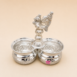 ASHTOK kumkum haldi holder with two silver-tone bowls and decorative peacock handle on beige background