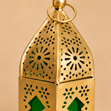 Detailed close-up image of the Ashtok Moroccan Lantern Candle Holder focusing on the upper portion of the lantern to highlight its craftsmanship and design details. The image clearly shows the gold metallic finish, pointed top structure, circular hanging ring, fine floral cut-out pattern work and the rich green glass visible through the decorative openings and window shapes. The close-up allows customers to inspect the texture, finishing quality, design precision and decorative appeal of the lantern more cl
