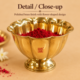 : High-angle detailed view of a polished brass flower-shaped kumkum bowl filled to the brim with bright red kumkum powder, displaying its scalloped edge contours and shiny metallic luster on a neutral beige background.