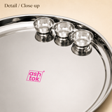Close-up detail of the smooth mirror finish and raised rim on the Ashtok stainless steel Mandi thali with three matching bowls.