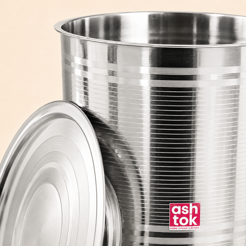 Close-up detail view of a glossy Ashtok stainless steel vertical storage container drum featuring horizontal line patterns and a matching steel lid leaning against its base.