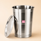 Ashtok stainless steel vertical storage container drum with horizontal line pattern texture and matching steel lid resting against the side.
