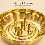 Close-up image of brass agarbatti stand showing polished brass craftsmanship, rounded tray design, incense holding tubes, smooth reflective finish and neat detailing, captured on a beige background for product detail emphasis.