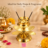 LifeStyle image of Brass agarbatti stand with lotus-style petal design, multiple incense stick holes and polished brass finish on a beige background.