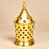Detailed close-up photograph of a traditional Brass Akhand Diya highlighting its polished golden brass conical lid, sacred Swastik-shaped cutouts, circular ventilation openings, finely machined decorative grooves, and ornamental pointed finial. The close-up also reveals the upper section of the cylindrical perforated brass enclosure with evenly spaced round holes and a reflective metallic finish. The intricate detailing gives this 7-inch brass Akhand Jyoti lamp an elegant traditional appearance suitable for