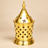 Traditional Brass Akhand Diya featuring a polished golden brass finish, decorative conical removable lid with sacred Swastik symbols, circular ventilation openings, elegant pointed finial, cylindrical perforated outer body, and a wide stepped pedestal base. Measuring 7 inches in height and 3.5 inches in diameter, this brass Akhand Jyoti lamp is designed for home mandir worship, daily pooja, Navratri celebrations, Diwali rituals, religious ceremonies, and traditional devotional arrangements. Displayed agains