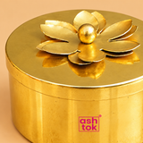 Open view of a decorative brass coloured metal dry fruit storage box featuring a smooth round golden container filled with almonds, cashews, pistachios and golden raisins. The removable circular lid is placed beside the box, showcasing its decorative raised flower-shaped handle and polished brass-coloured finish. The image highlights the single-compartment storage design for dry fruits, sweets and festive gift arrangements.