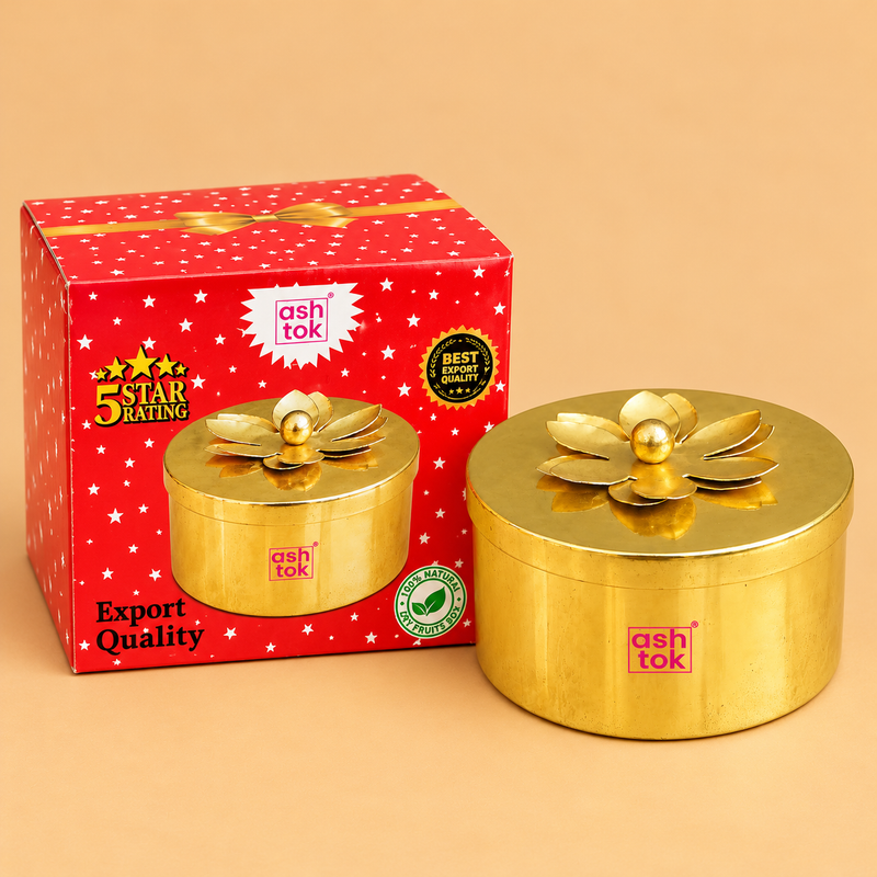 Traditional brass coloured metal dry fruit gift box featuring a smooth cylindrical storage container, polished golden metallic finish and a matching removable circular lid decorated with a raised flower-shaped ornament and central golden knob. The compact round gift box measures 4 inches in diameter and 2 inches in height, making it suitable for storing dry fruits, sweets, wedding return gifts, festive gifting and decorative household accessories.