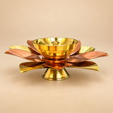 Decorative brass and copper lotus diya shown from the front on a premium beige studio background, featuring layered metallic lotus petals in alternating golden brass and warm copper tones, a polished central brass oil bowl with wick holder, and a stable golden pedestal base, photographed in a clean ecommerce style to highlight the reflective metal finish, floral construction and traditional design suitable for daily puja, festive worship, Diwali decor, home mandir use, religious ceremonies and traditional g