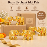 Bulk gifting presentation of multiple Brass Elephant Idol Pairs arranged with simple cardboard gift packaging against a premium beige studio background. Each set contains two golden elephant figurines featuring raised trunks, polished reflective brass surfaces, intricate ornamental carvings and decorative traditional patterns. Every elephant measures 2 inches in length, 1 inch in width and 1.5 inches in height. These miniature brass elephant sets are suitable for wedding return gifts, housewarming gifts.