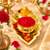 Traditional brass Haldi Kumkum bowl set with two golden brass containers holding yellow haldi and red kumkum on a decorative leaf-shaped tray. Displayed in a festive pooja setting with a lit brass diya, jasmine flowers, red roses and traditional accessories. Suitable for daily puja, Varalakshmi Vratham, weddings and religious celebrations.